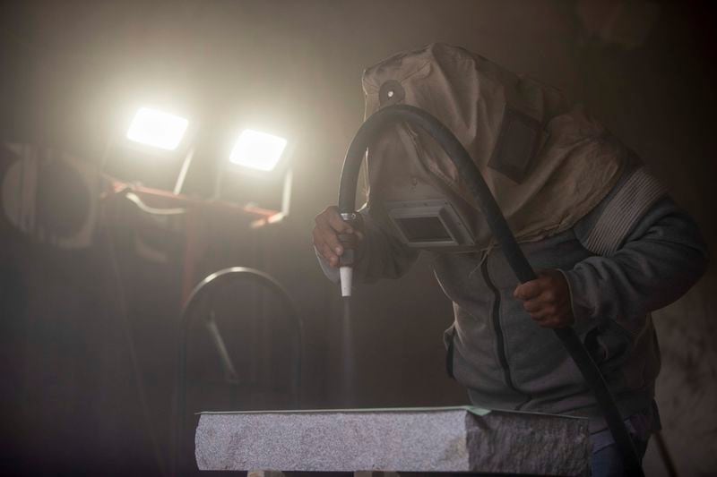 Mario Badillo wears protective gear while using a sandblaster to carve out a message for a gravestone while working at The Engraving House in Lithonia, Thursday, October 7, 2021. (Alyssa Pointer/ Alyssa.Pointer@ajc.com)