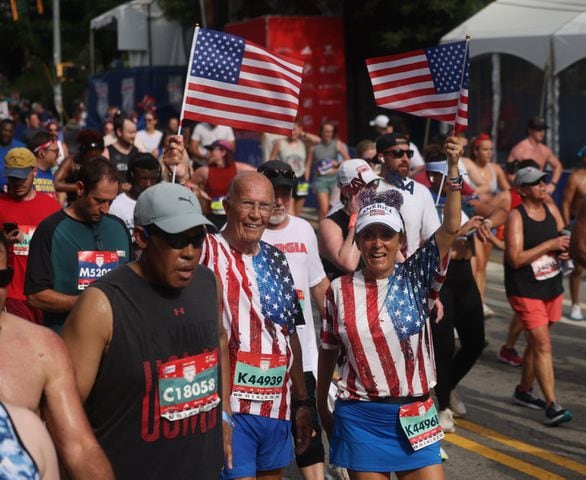 John Howard and Bettilee Miller wave flags at the finish of the 55th running of the Atlanta Journal-Constitution Peachtree Road Race in Atlanta on Thursday, July 4, 2024.   (Jason Getz / AJC)