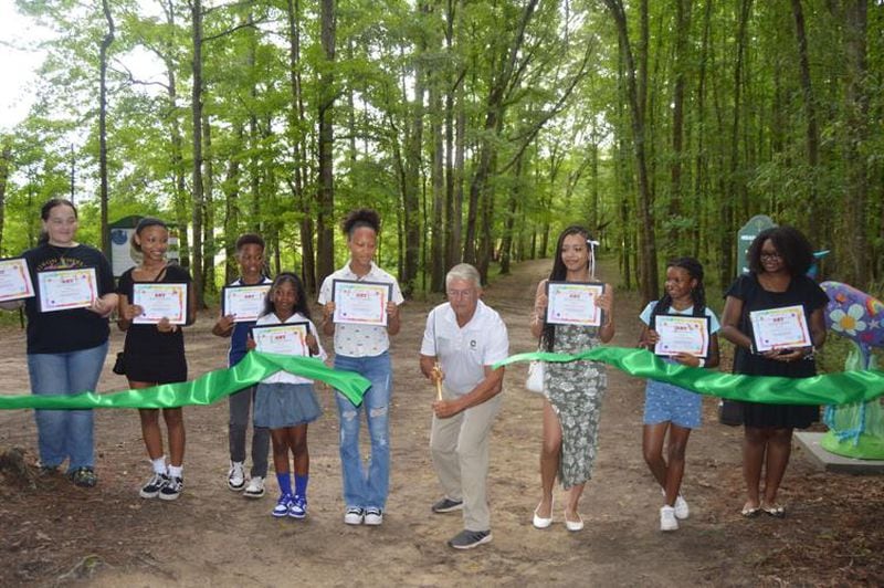 Conyers Mayor Vince Evans cuts the ribbon for the new Herald of Herons exhibit at the Big Haynes Nature Center. Standing next to the mayor are some of the young artists who created the designs for the heron statues. (Photo Courtesy of Alice Queen)