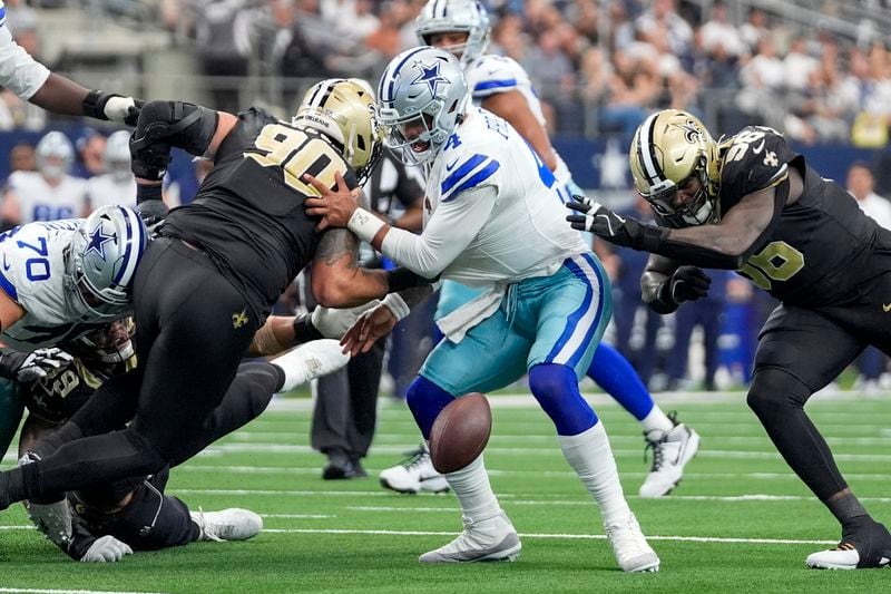 Dallas Cowboys quarterback Dak Prescott, center, fumbles the ball while being pressured by New Orleans Saints defensive tackle Bryan Bresee (90) and defensive end Carl Granderson (96) during the second half of an NFL football game, Sunday, Sept. 15, 2024, in Arlington, Texas. (AP Photo/Tony Gutierrez)