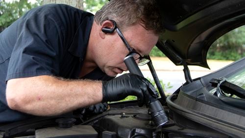 Kevin Keller inspects the inside of a car with a flashlight to make sure there is no oil leak in a parking lot in Roswell on Monday, July 12, 2021. Keller, a technicians for YourMechanic.com, will meet customers where they want their services done, but he has had trouble getting needed parts. (Christine Tannous / christine.tannous@ajc.com)