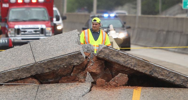 April 17, 2017, Atlanta, Georgia - A crew member glances through the large rift in I-20 WB after the road buckled that morning in Atlanta, Georgia, on April 17, 2017. On the morning of April 17th a section of I-20 WB near the Gresham Road exit buckled. According to Dekalb County Fire Department PIO Eric Jackson there were private contractors working on a gas pipe running underneath the interstate. The private contractors were filling the pipe with cement when pressure started building up. According to Jackson the buckle acted as a pressure release valve. According to WSB-TV, they were told the rise of concrete was gradual and not sudden. In addition to all west bound lanes being closed while crews assess the situation, a motorcyclist may have crashed after running into the buckle, the driver of the motorcycle was taken to a local area hospital. (HENRY TAYLOR / HENRY.TAYLOR@AJC.COM)