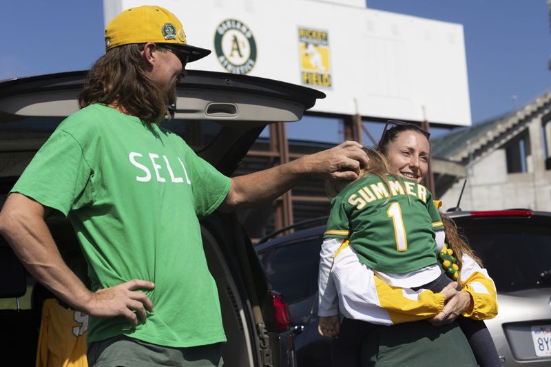 Jacob Sutter, left, stands as Marta Sutter holds their daughter, 3-year-old Summer Sutter outside the Oakland Coliseum before a baseball game between the Oakland Athletics and the Texas Rangers Thursday, Sept. 26, 2024, in Oakland, Calif. (AP Photo/Benjamin Fanjoy)