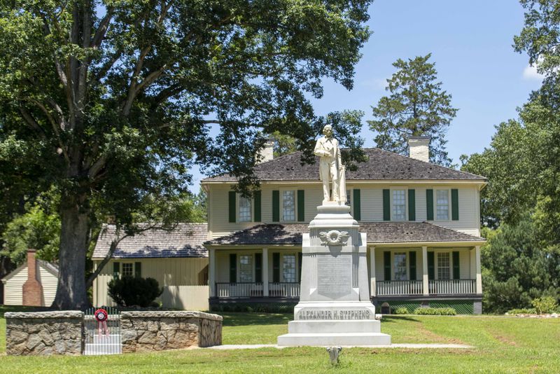 A statue of Alexander Hamilton Stephens, former vice president of the Confederacy, is displayed near his burial plot (left) and his former home at A.H. Stephens State Park in Crawfordville, Georgia on Monday, July 13, 2020. (ALYSSA POINTER / ALYSSA.POINTER@AJC.COM)