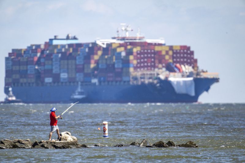 The container ship Dali approaches the Chesapeake Bay Bridge, Monday, June 24, 2024, on its way to Norfolk, Va., as a man fishes at Sandy Point State Park. Ninety days ago the ship hit a support pier of the bridge causing a catastrophic collapse. (Jerry Jackson/The Baltimore Sun via AP)