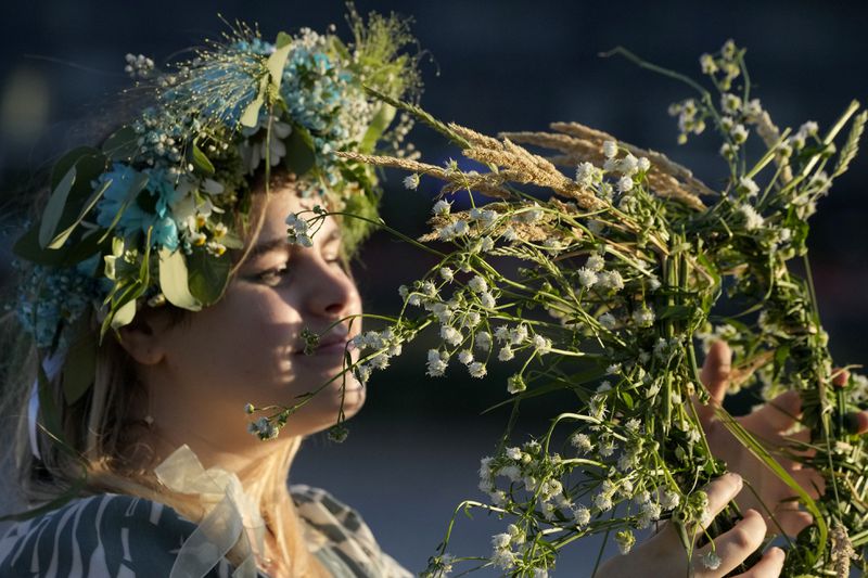 A young Ukrainian woman wearing an ear of grain braid holds grain and flowers during a traditional Ukrainian celebration of Kupala Night, in Warsaw, Poland, on Saturday, June 22, 2024. Ukrainians in Warsaw jumped over a bonfire and floated braids to honor the vital powers of water and fire on the Vistula River bank Saturday night, as they celebrated their solstice tradition of Ivan Kupalo Night away from war-torn home. (AP Photo/Czarek Sokolowski)