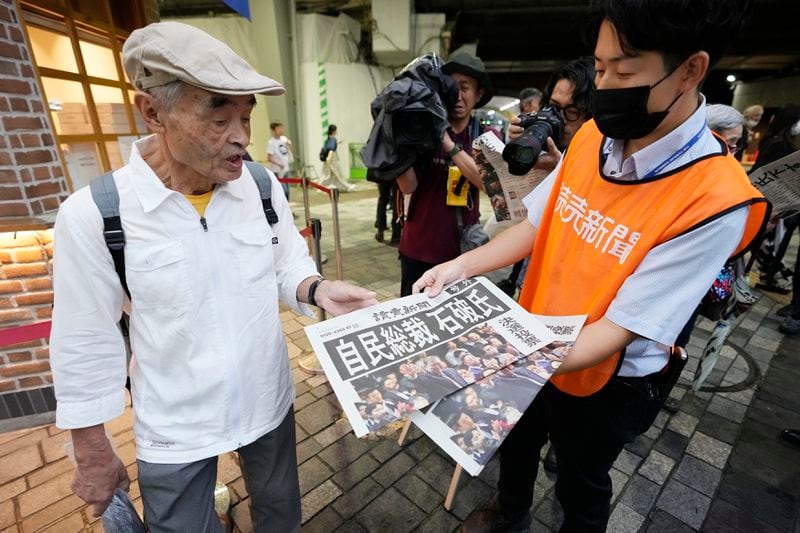 A pedestrian takes a copie of an extra edition of the Yomiuri newspaper reporting on Shigeru Ishiba becoming the winner of the Liberal Democratic Party's presidential election Friday, Sept. 27, 2024, in Tokyo. (AP Photo/Hiro Komae)