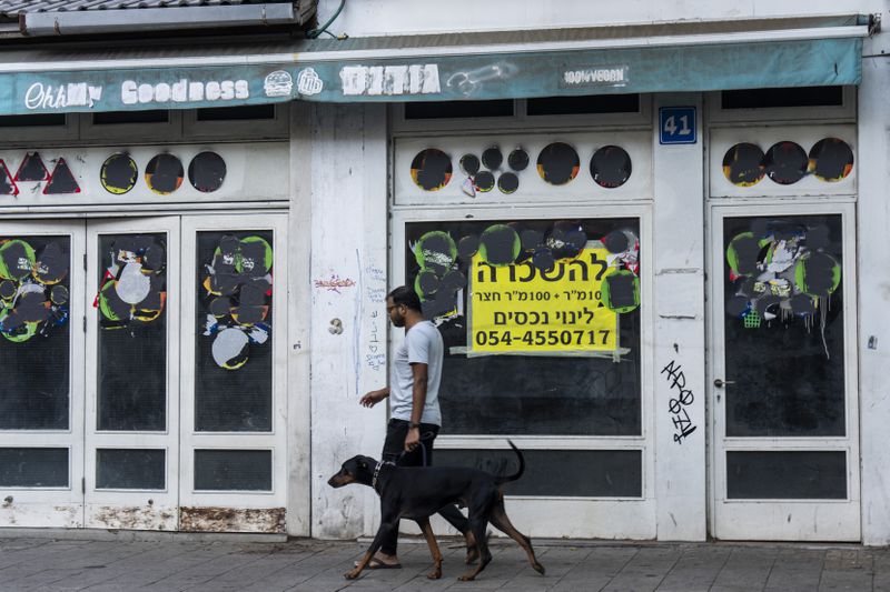 A person walks his dog past a closed shop to rent in Tel Aviv, Israel, Thursday, Aug. 15, 2024. Israel's economy is suffering from the nearly 11-month war with Hamas, as its leaders grind ahead with its offensive in Gaza that threatens to escalate into a wider conflict. (AP Photo/Ariel Schalit)