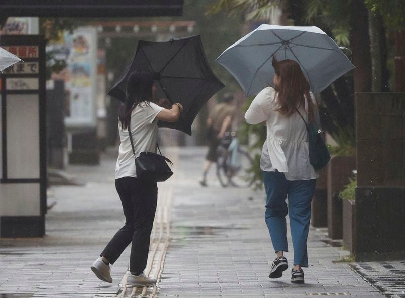 People holding umbrella, struggle with the strong wind as a typhoon is approaching in Kagoshima, western Japan, Tehursday, Aug. 29, 2024, (Hidetaka Komukai/Kyodo News via AP)