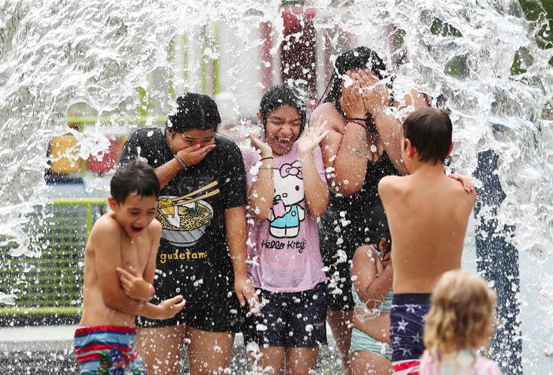 Yezica Jimenez, 16, from left, Luzmaria Celis, 13, and Sandra Cortez stand under a water barrel at the splash pad inside Waterfront Park in Louisville, Ky., on Tuesday, June 18, 2024. Louisville is expected to have sustained temperatures in the 90's all week. (Sam Upshaw Jr./Courier Journal via AP)