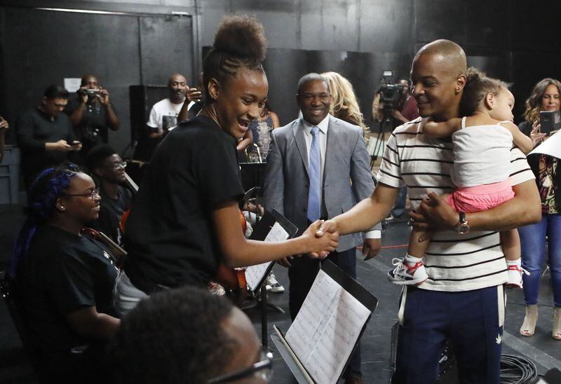 Lailah Carter, from Carver Early College in Atlanta, stands as students are greeted by T.I., holding his daughter, as he arrives for rehearsal Wednesday for a live concert. BOB ANDRES / BANDRES@AJC.COM