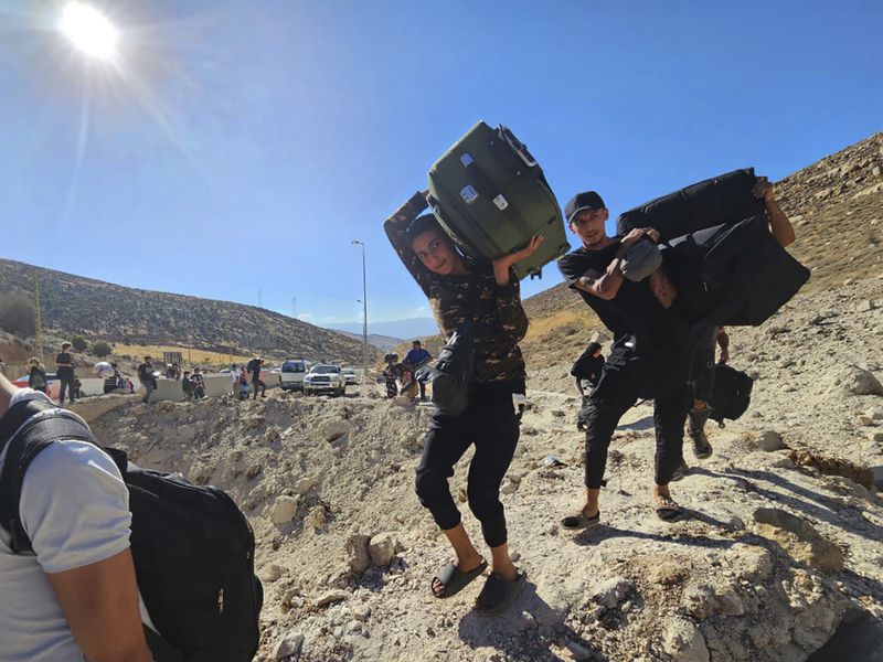 Syrians carry their luggages as they cross on foot into Syria through a crater caused by an Israeli airstrike to cut the road between the Lebanese and the Syrian checkpoints, at the Masnaa crossing, in the eastern Bekaa Valley, Lebanon, Friday, Oct. 4, 2024. (AP Photo/Samer Husseini)