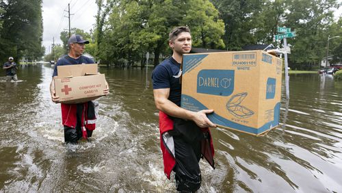 Savannah Fire Advanced Firefighters Ron Strauss, right, and Andrew Stevenson, left, carry food to residents in the Tremont Park neighborhood that where stranded in flooding from Tropical Storm Debby, Tuesday, Aug. 6, 2024, in Savannah, Ga. (AP Photo/Stephen B. Morton)