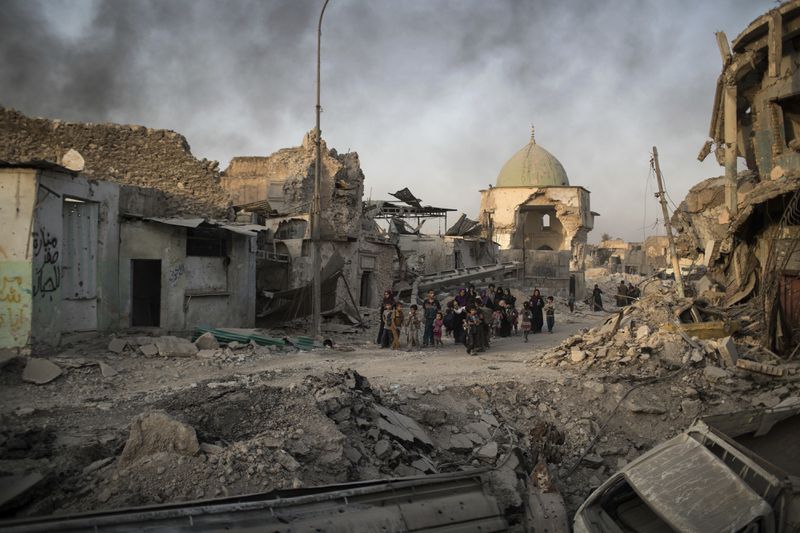 File - Fleeing Iraqi civilians walk past the heavily damaged al-Nuri mosque as smoke rises in the background in the Old City of Mosul, Iraq, Tuesday, July 4, 2017. The United Nations cultural agency has discovered five bombs hidden within the walls the historic al-Nouri Mosque in the city of Mosul in northern Iraq, a remnant of the Islamic State militant group's rule over the area, UNESCO said in a statement Saturday, June 29, 2024. (AP Photo/Felipe Dana, File)