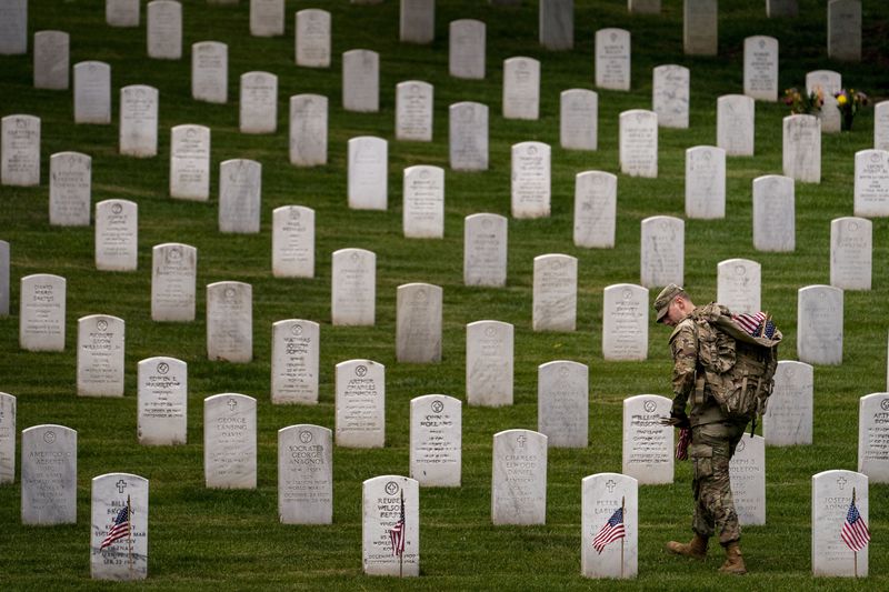 FILE - A member of the 3rd U.S. Infantry Regiment also known as The Old Guard, places flags in front of each headstone for "Flags-In" at Arlington National Cemetery in Arlington, May 25, 2023, to honor the Nation's fallen military heroes ahead of Memorial Day. Memorial Day is supposed to be about mourning the nation’s fallen service members. But it’s come to anchor the unofficial start of summer and retail discounts. (AP Photo/Andrew Harnik, file)