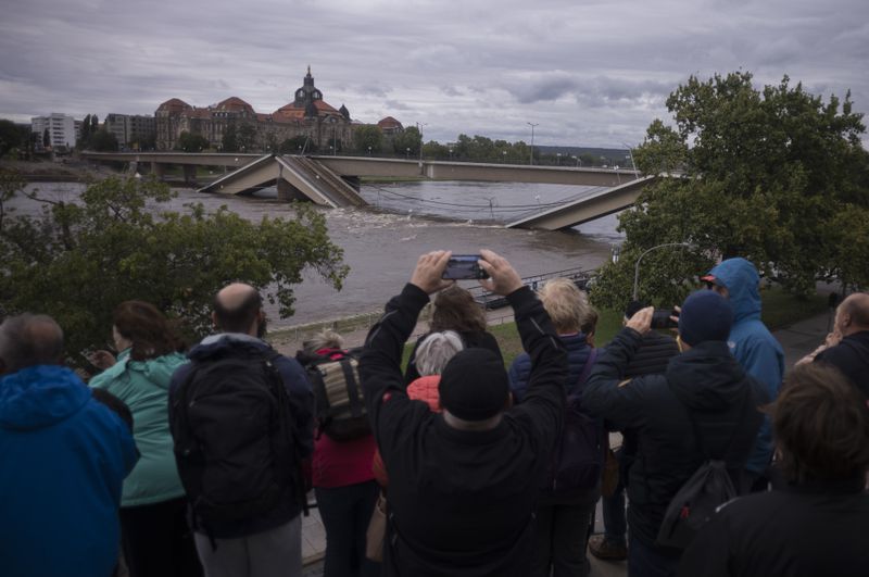 Spectators look at the partially collapsed Carolabrücke bridge over the Elbe, which is rising rapidly due to upcoming flood waters, in front of the state chancellery in Dresden, Germany, Sunday, September 15, 2024. (AP Photo/Markus Schreiber)