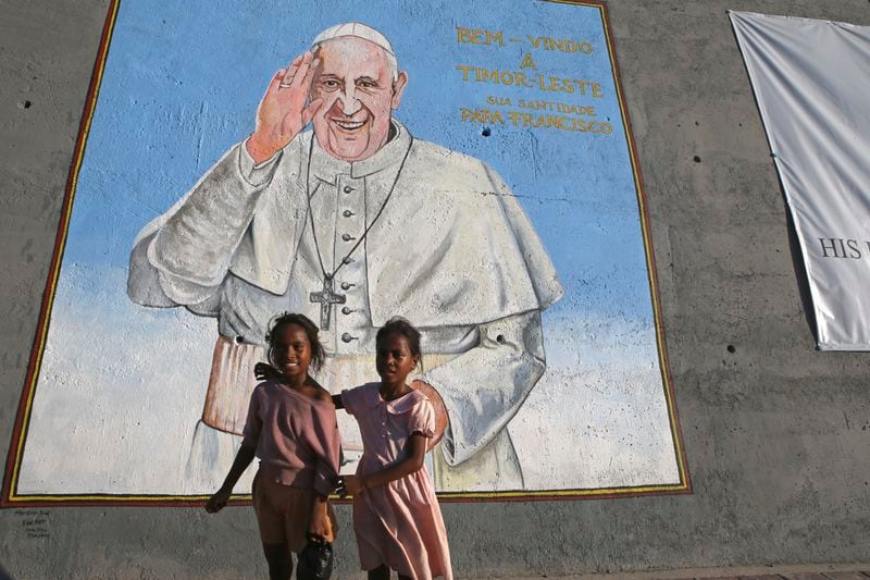 Girls stand in front a wall photo welcoming Pope Francis in Dili, East Timor on Tuesday, Sept. 3, 2024. (AP Photo/Firdia Lisnawati)