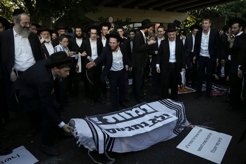 Ultra-Orthodox Jewish men stand in front of a coffin with a banner that reads in Hebrew "We'll die and not go to the army", as they block a highway during a protest against army recruitment in Bnei Brak, Israel, Thursday, June 27, 2024. Israel's Supreme Court unanimously ordered the government to begin drafting ultra-Orthodox Jewish men into the army — a landmark ruling seeking to end a system that has allowed them to avoid enlistment into compulsory military service. (AP Photo/Oded Balilty)