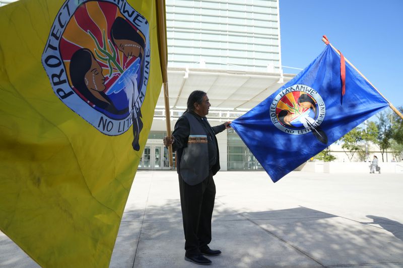 Frank Mapatis holds up flags as he joins other members of the Hualapai Tribe as they gathered in protest to try to persuade a federal judge to extend a temporary ban on exploratory drilling for a lithium project at U.S. District Court Tuesday, Sept. 17, 2024, in Phoenix. (AP Photo/Ross D. Franklin)