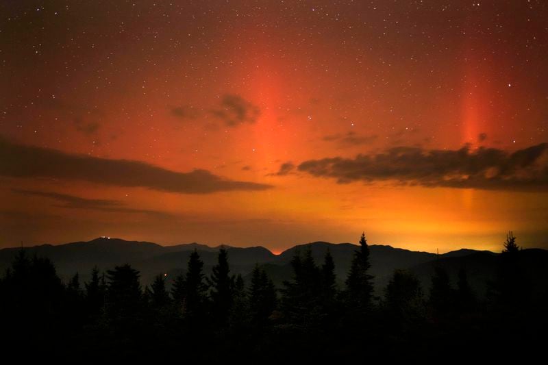 Flares of northern lights color the sky over the White Mountains just after midnight, Friday, Sept. 13, 2024, as viewed from mountaintop in Chatham, N.H. Lights on the summit of Mount Washington can be seen on the ridgeline at left. (AP Photo/Robert F. Bukaty)