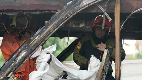 Rescuers hold a white cloth to cover the body of a victim inside a bus that caught fire, carrying young students with their teachers, in suburban Bangkok, Tuesday, Oct. 1, 2024. (AP Photo/Sakchai Lalit)