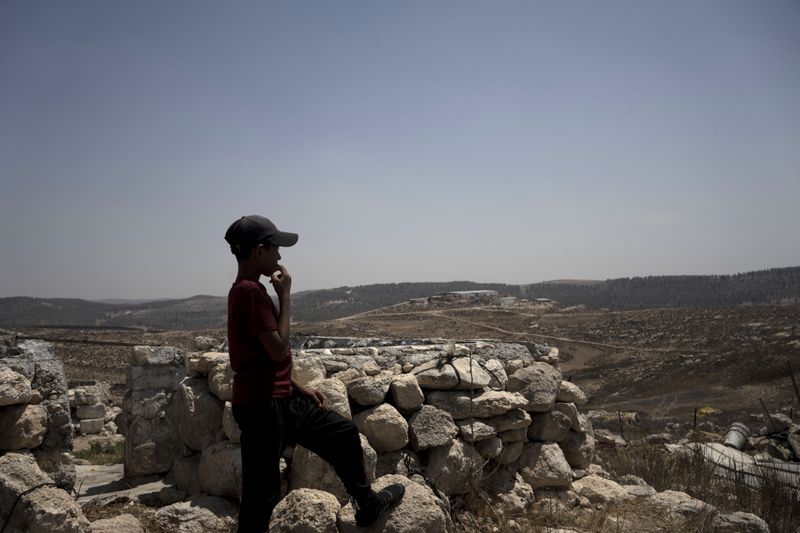 A child stands in the ruins of a stone house in the West Bank village of Khirbet Zanuta, overlooking the Meitarim Farm, owned by sanctioned settler Yinon Levy Tuesday, Aug. 27, 2024. The Palestinian community was driven out by Israeli settlers but a handful of residents have returned under court order. (AP Photo/Maya Alleruzzo)