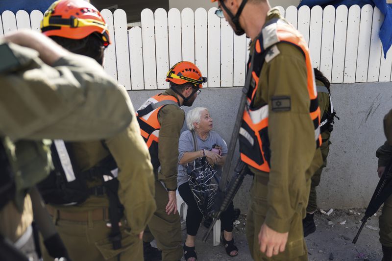 Israeli soldiers from the Homefront Command unit treat an elderly woman at the site that was hit by a rocket fired from Lebanon, in Kiryat Yam, northern Israel, on Tuesday, Oct. 8, 2024. (AP Photo/Ariel Schalit)