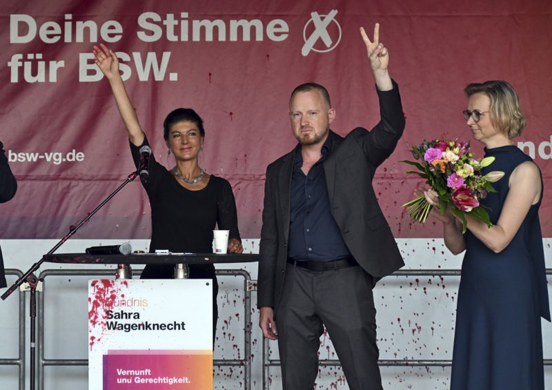 Sahra Wagenknecht, left, Chairwoman of the Sahra Wagenknecht Alliance (BSW), Katja Wolf, Thuringian BSW State Chairwoman and top candidate for the state election in Thuringia 2024, and Christian Leye, BSW General Secretary, stand together on stage after an attack with red paint at the election campaign event on Domplatz, in Erfurt, Germany, Thursday Aug. 29, 2024. (Martin Schutt/dpa via AP)