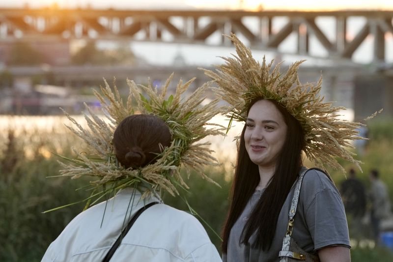 Young Ukrainian women wear ear of grain braids during a traditional Ukrainian celebration of Kupala Night, in Warsaw, Poland, on Saturday, June 22, 2024. Ukrainians in Warsaw jumped over a bonfire and floated braids to honor the vital powers of water and fire on the Vistula River bank Saturday night, as they celebrated their solstice tradition of Ivan Kupalo Night away from war-torn home. (AP Photo/Czarek Sokolowski)