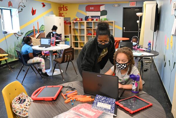 Mayai Carthans, program facilitator, helps Micaela McClesky, 7, with her school online class as students complete their online classes at Girls Inc. in Marietta on August 19. (Hyosub Shin / Hyosub.Shin@ajc.com)