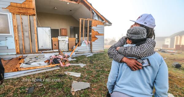 Ontario Alvarez hugs his mother, Katrina Dawson, outside their home on Jumpers Trail. JOHN SPINK / AJC