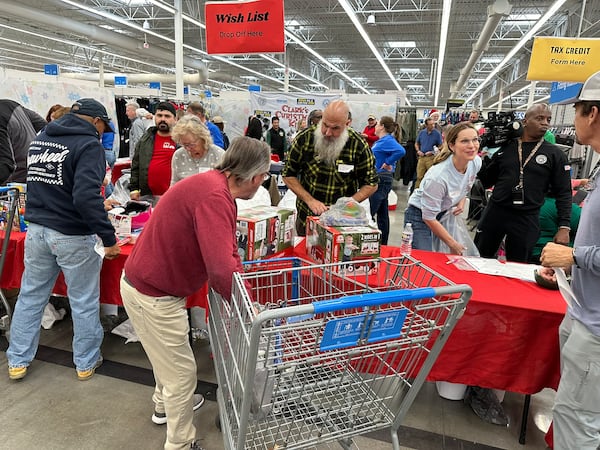 Jim Recznik, in the beard, volunteered to take gifts from shoppers as part of Clark's Christmas Kids at Roswell's Walmart Dec. 8, 2024. Lane Howard, Clark Howard's wife, is on the right. RODNEY HO/rho@ajc.com