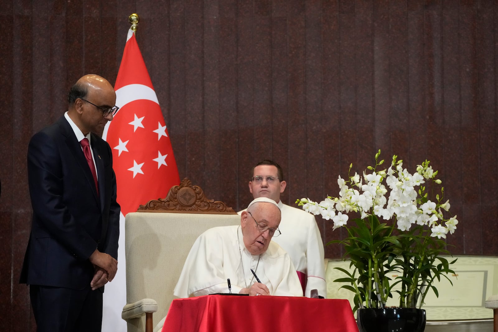 Pope Francis signs the book of honor during a welcome ceremony with the President of the Singapore Republic Tharman Shanmugaratnam, left, at the Parliament House in Singapore, Thursday, Sept. 12, 2024. Pope Francis flew to Singapore on Wednesday for the final leg of his trip through Asia, arriving in one of the world's richest countries from one of its poorest after a record-setting final Mass in East Timor. (AP Photo/Gregorio Borgia)