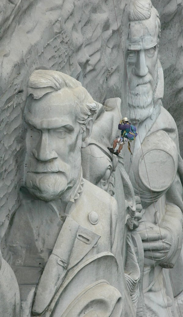 A climber dangles between the granite carvings of General Robert E. Lee (left) and General Stonewall Jackson as he rappels across the memorial. AJC file photo, 2002.