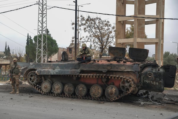 A Syrian opposition fighter reads while sitting atop a damaged government armoured vehicle near Hama, Syria, on Saturday, Dec. 7, 2024. (AP Photo/Ghaith Alsayed)