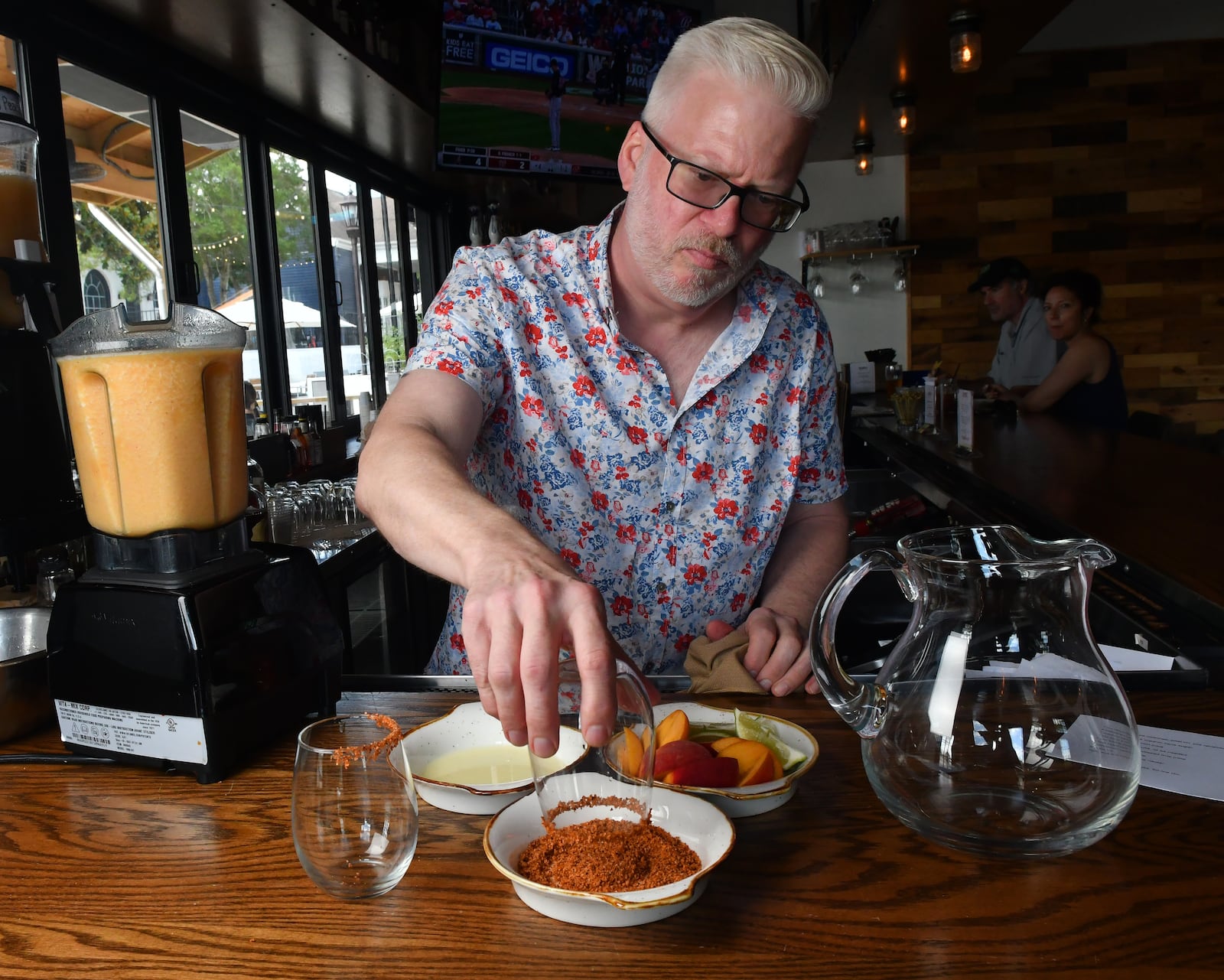 Phil Handley, a partner with DASH Hospitality Group, rims the glasses for Bar(n) Booze (n) Bites' The Spicy Peach Margarita with Tajin. You can choose how much Tajin to use on the rim of the drink, a frozen combination that includes peach puree, tequila, lime juice and agave nectar. (Styling by Phil Handley / Chris Hunt for the AJC)