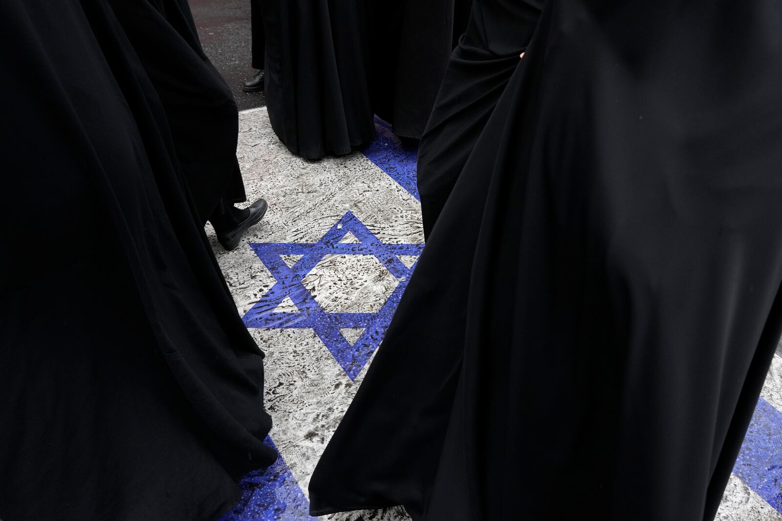 Women walk on an image of the Israeli flag put on the street in an annual rally in front of the former U.S. Embassy in Tehran, Iran, Sunday, Nov. 3, 2024, marking the 45th anniversary of Iranian students' takeover of the embassy, starting a hostage crisis. (AP Photo/Vahid Salemi)