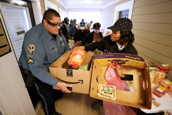 Community affairs officer Christian Matos, from Gwinnett P. D., helps to put food in a box for Tiffany Miller at Bradford Gwinnett apartment complex during a community outreach event on Thursday, Feb 2, 2023. Miguel Martinez / miguel.martinezjimenez@ajc.com