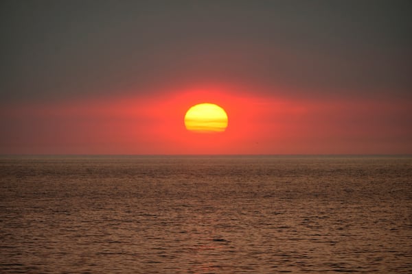 The sun sets under a plume of smoke from the Franklin Fire rising over the ocean Tuesday, Dec. 10, 2024, in Malibu, Calif. (AP Photo/Damian Dovarganes)