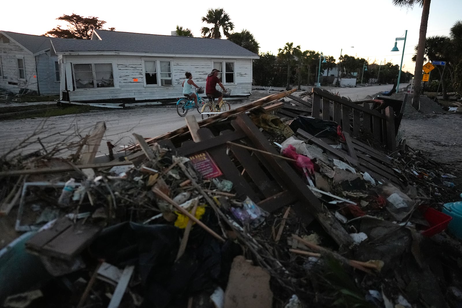 People bike past damaged homes and debris left by Hurricane Milton, on the sand-coated main road of southern Manasota Key, already cleared of feet of sand, in Englewood, Fla., Sunday, Oct. 13, 2024. (AP Photo/Rebecca Blackwell)