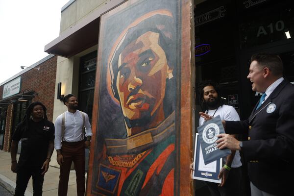 Iron Palm Tattoos owner Marlon Blake (from left), Atlanta Ink owner Christian Verrette, and tattoo artist J.R. Outlaw listen as Guinness World Records employee Michael Empric, announces the world's largest tattoo reward for an art piece design of the late rapper Takeoff at Atlanta Ink in Atlanta on July 5, 2023. (Michael Blackshire/Michael.blackshire@ajc.com)