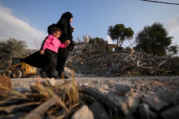 A woman with a child pass at the site where an Israeli airstrike hit a house in Aalmat village, northern Lebanon, Sunday, Nov. 10, 2024. (AP Photo/Hassan Ammar)