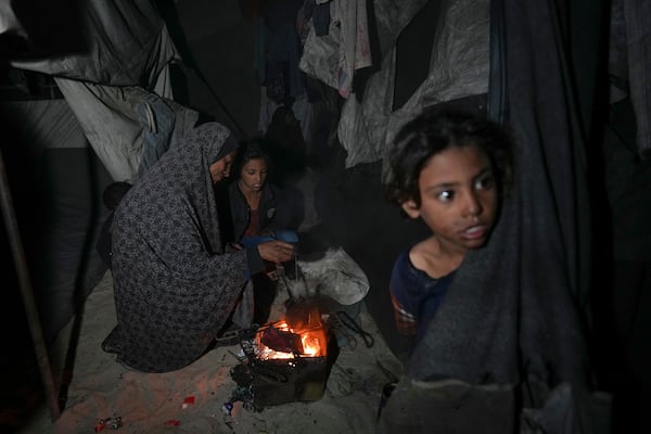 Shireen Daifallah, who was displaced with her children from northern Gaza, checks the fire next to their tent at a camp for displaced people in Deir al-Balah. Gaza Strip, Saturday, Nov. 30, 2024. (AP Photo/Abdel Kareem Hana)