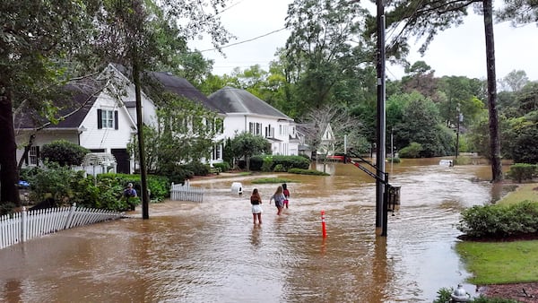 Teenagers walk in floodwaters covering a street in the Hanover West neighborhood Friday after heavy rains from Tropical Storm Helene drenched the region. (Miguel Martinez / AJC)