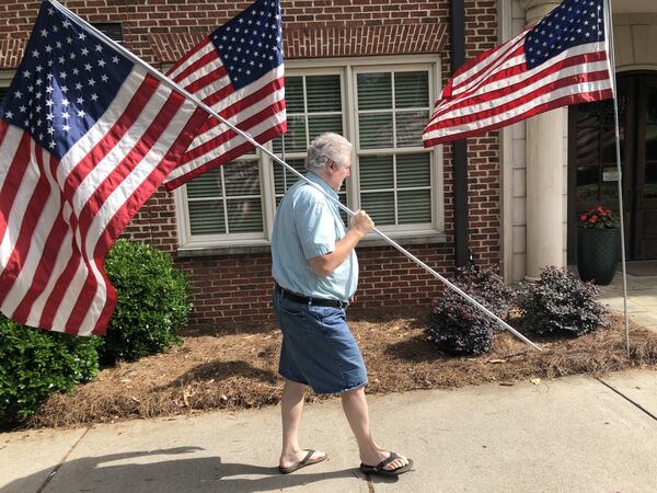 Daniel Creager, of Marietta, puts up American flags outside a condo building on Washington Avenue near the Marietta National Cemetery on Saturday, May 23, 2020. The coronavirus halted many Memorial Day weekend ceremonies and traditions, including the annual day of service by members of the Boy Scouts of putting flags at each grave stone in the cemetery. J. SCOTT TRUBEY/STRUBEY@AJC.COM