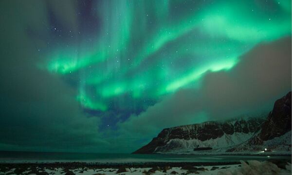 Northern lights ( aurora borealis ) illuminated the sky over a snow covered beach in the Arctic Circle in March of 2016. 