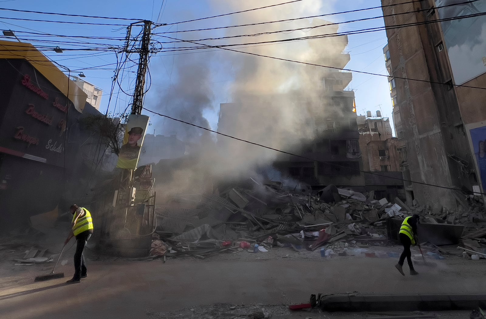 Workers clean a street as smoke rises from a destroyed building that was hit by an Israeli airstrike in Dahiyeh, a southern suburb of Beirut, Lebanon, early Sunday, Oct. 20, 2024. (AP Photo/Hussein Malla)