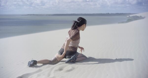 Choreographer and dancer Mami Kang moves slowly and effortfully through the sand in one scene from "Songs from the Compost."