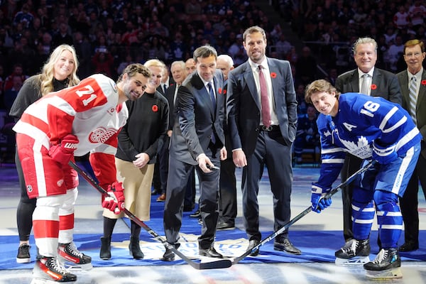 2024 Hockey Hall of Fame inductees Krissy Wendell-Pohl, back left to right, Natalie Darwitz, Pavel Datsyuk, Shea Weber, Jeremy Roenick and David Poile pose for a ceremonial face-off photo with Detroit Red Wings' Dylan Larkin (71) and Toronto Maple Leafs' Mitch Marner (16) during a pre-game ceremony prior to NHL hockey action in Toronto on Friday, November 8, 2024. (Frank Gunn/The Canadian Press via AP)