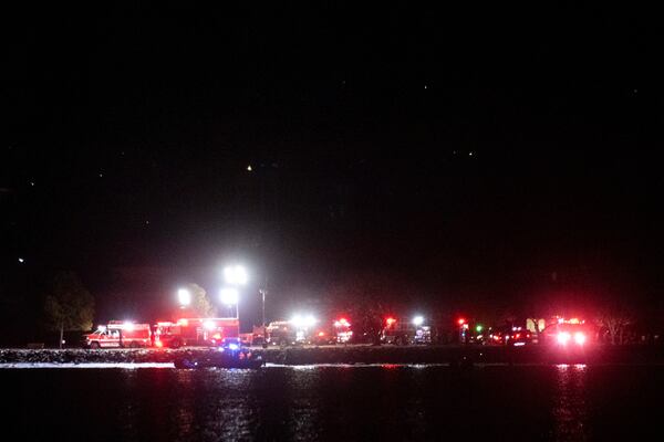 A boat on the Potomac River, cruises past emergency response vehicles seen staging at Joint Base Anacostia Bolling, in the early morning hour, Thursday, Jan. 30, 2025 in Washington, as seen from across the river near Ronald Reagan Washington National Airport in Arlington, Va. (AP Photo/Kevin Wolf)